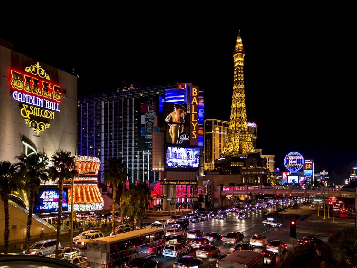 Nighttime image of the Las Vegas Strip with brightly lit hotels, casinos, and the Eiffel Tower replica. Bustling street traffic below.