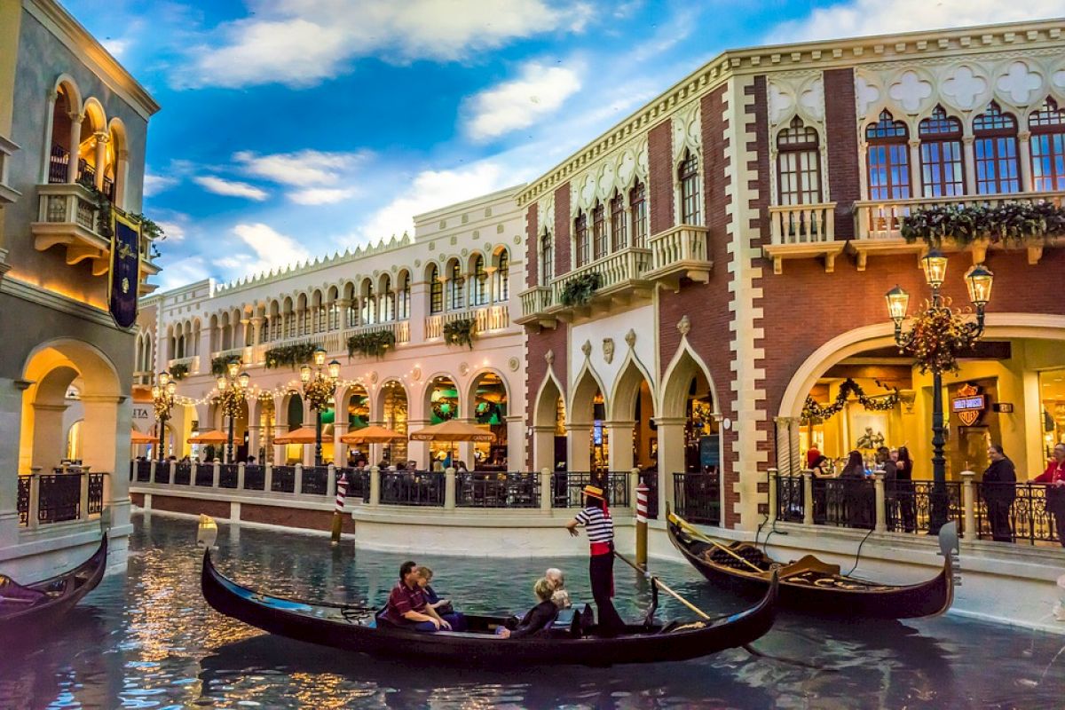 A picturesque canal scene with gondolas and gondoliers, surrounded by Venetian-style architecture and shops, possibly in an indoor setting.