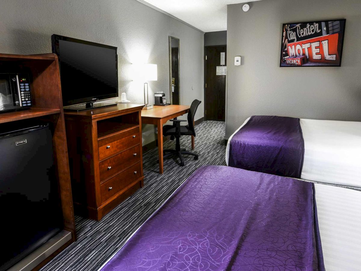 The image shows a hotel room with two beds, a TV on a dresser, a mini-fridge, a desk with a chair, and a wall-mounted sign reading "Motel".