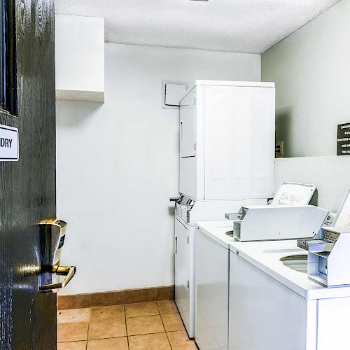 This image shows a guest laundry room with washing machines and dryers, a clock on the wall, and a sign on the door reading 