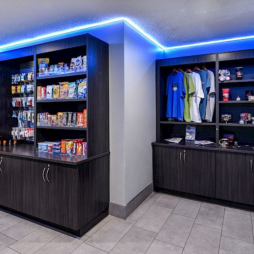 The image shows shelves displaying various snacks, drinks, and merchandise under blue LED lighting in a modern store setting.