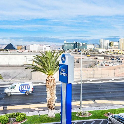 An urban landscape with palm trees, a Best Western sign, a white van, and buildings, including a black pyramid, set against a blue sky.