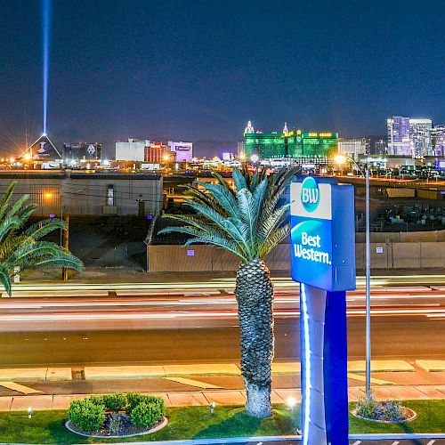 A night view of a cityscape featuring a street with palm trees, a 