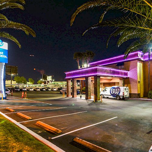 The image shows a Best Western hotel at night, with palm trees, parking spaces, and cars in a well-lit, welcoming setting.