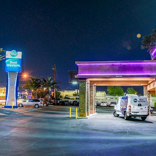 This is a nighttime view of a Best Western hotel, featuring palm trees and a lit-up sign near the entrance with a van parked outside.