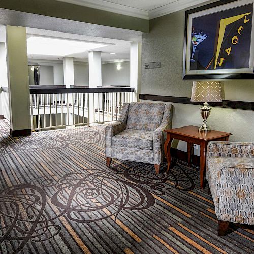 This image shows a hotel hallway with two armchairs, a side table with a lamp, a framed picture on the wall, and a vending machine in the background.