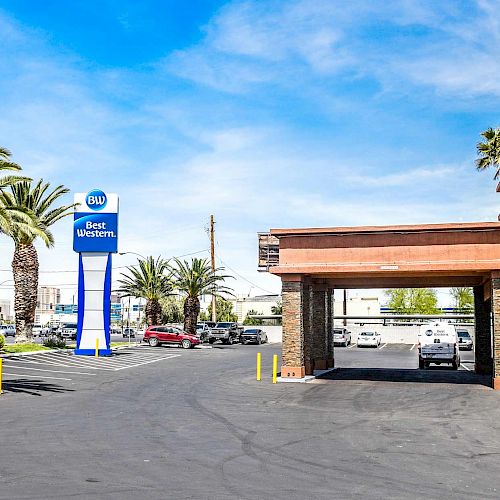 The image shows a Best Western hotel entrance with palm trees in the parking lot, a clear sky, and some cars in the background.