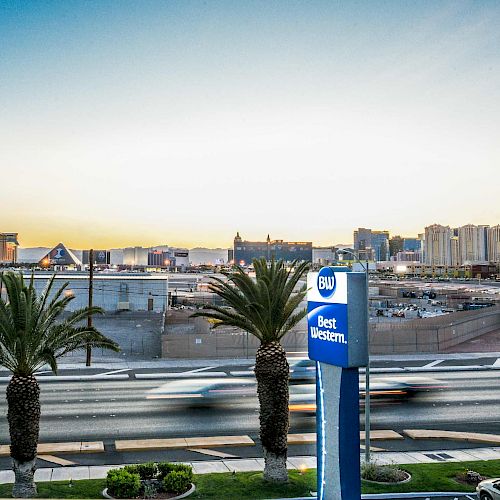 The image features a cityscape at sunset with a Best Western sign in the foreground, palm trees, and distant buildings under a clear sky ending the sentence.