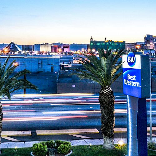 The image shows a Best Western hotel sign with palm trees in the foreground, and a cityscape with various buildings and lights in the background.