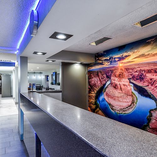 The image shows a modern indoor setting with a long counter and a large wall mural of a scenic canyon landscape.