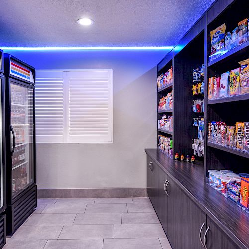 The image shows a modern snack room with shelves stocked with various snacks and refrigerated items. The area is well-lit with blue accent lighting.