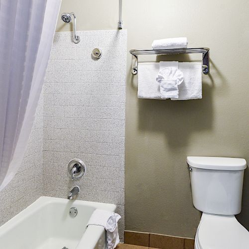 A clean bathroom with a bathtub, shower curtain, toilet, and a towel shelf holding folded towels and a towel shaped like a swan.