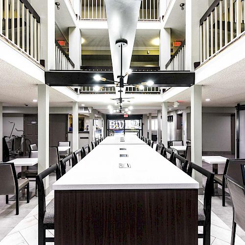 A modern dining area is shown with tables, chairs, a large central table, and an upper level with railings visible above.