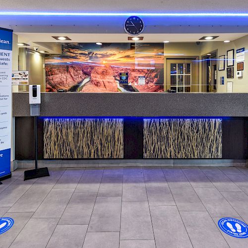 This image shows a hotel reception area with a banner, plexiglass divider, and social distancing markers on the floor, ending the sentence.