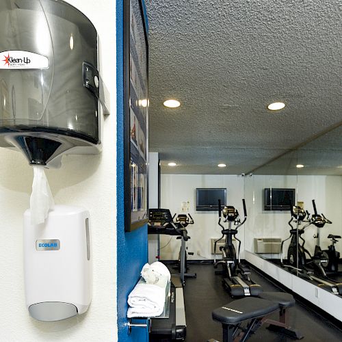 A gym with a mirror, exercise equipment, and sanitizing dispensers mounted on the wall.