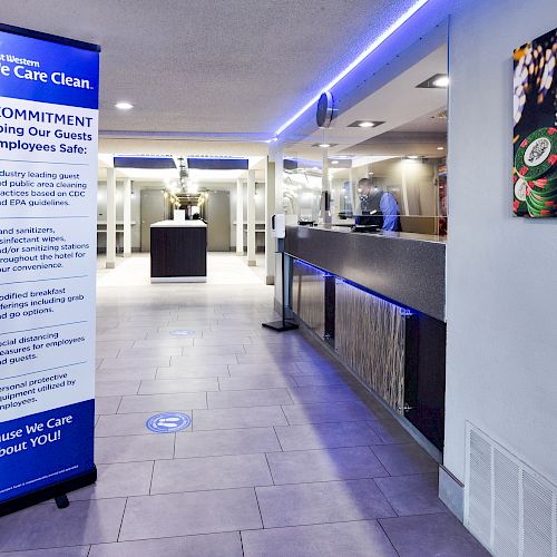 A hotel lobby with a health and safety commitment sign, emphasizing cleanliness for guest and employee safety, and a counter at the end.