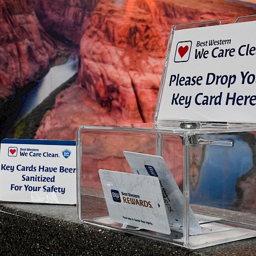 A transparent box with a 'Please Drop Your Key Card Here' sign, a separate note about sanitized key cards for safety, all placed on a counter.