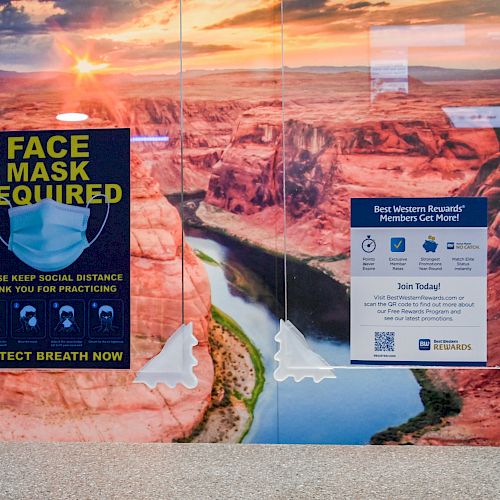 Two posters about face masks and social distancing are on a wall with a canyon background.