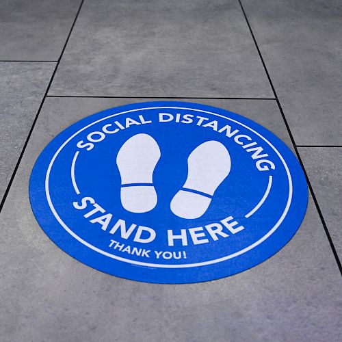 A blue floor sticker with footprints says 