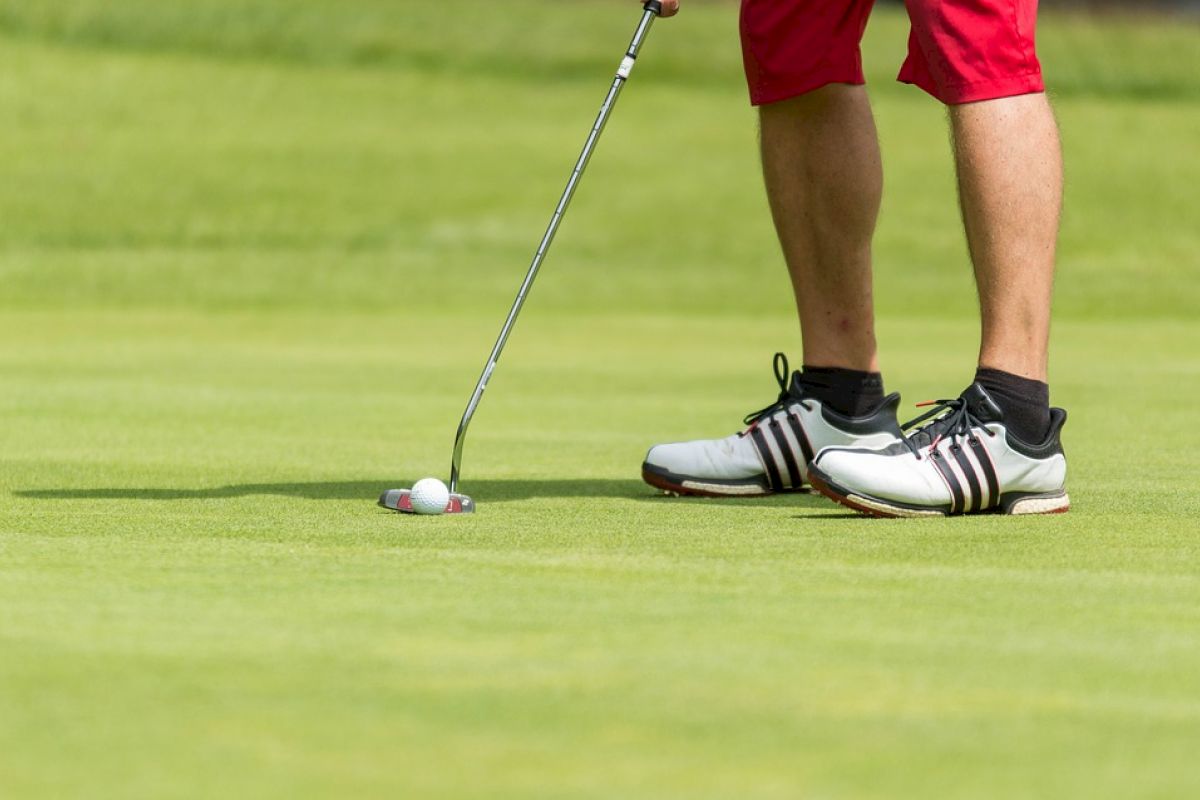 A golfer wearing red shorts and white shoes, preparing to putt the ball on the green, holding a putter.