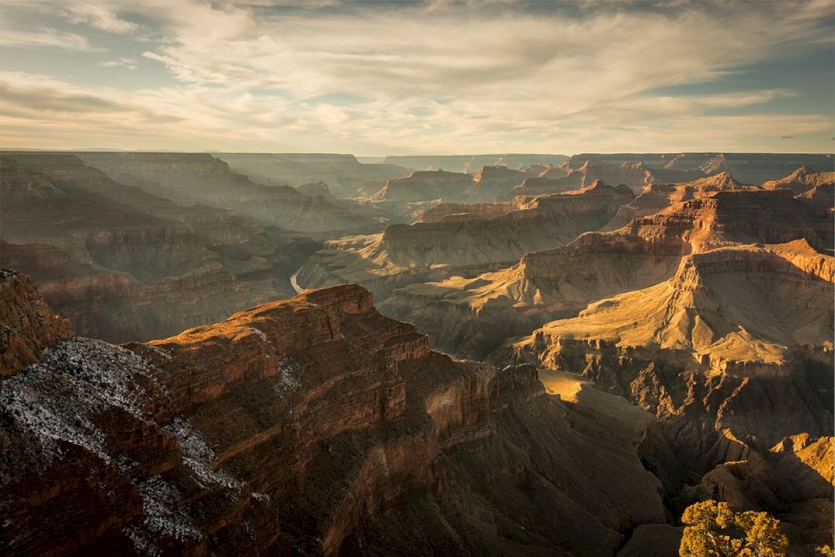 The image showcases a stunning landscape of the Grand Canyon with vast, layered rock formations under a partially cloudy sky during sunset.