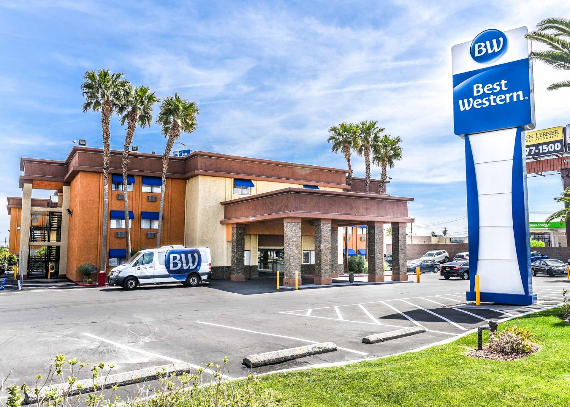 The image shows a Best Western hotel with a marked van, a large sign, and palm trees nearby under a blue sky.