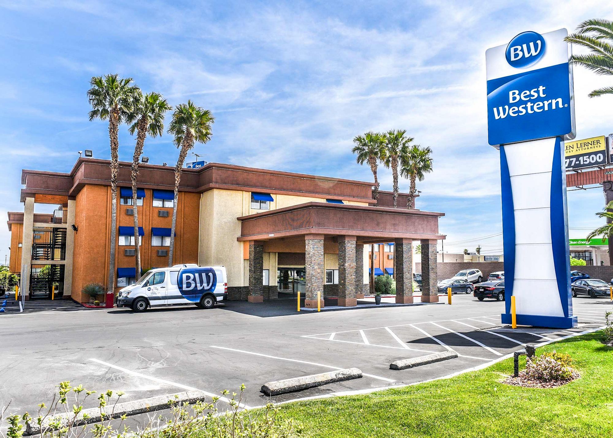 The image shows a Best Western hotel with a marked van, a large sign, and palm trees nearby under a blue sky.