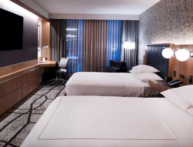 A modern hotel room with two neatly-made beds, a wall-mounted TV, a desk and chair by the window, and stylish wall decor ending the sentence.