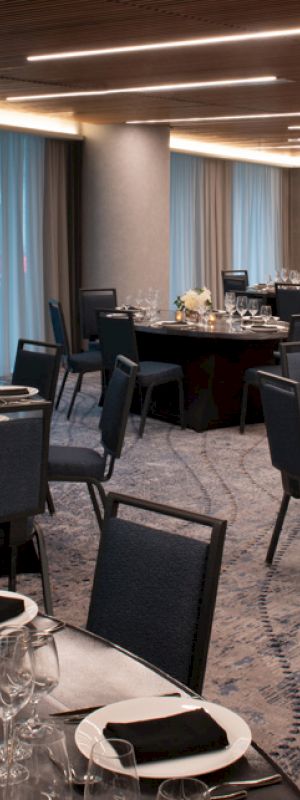 The image shows an elegant banquet hall with round tables, set with black napkins, plates, wine glasses, and centerpiece decorations.