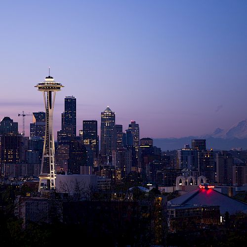 This image shows the Seattle skyline at dusk, featuring the Space Needle prominently, with Mount Rainier in the distant background.