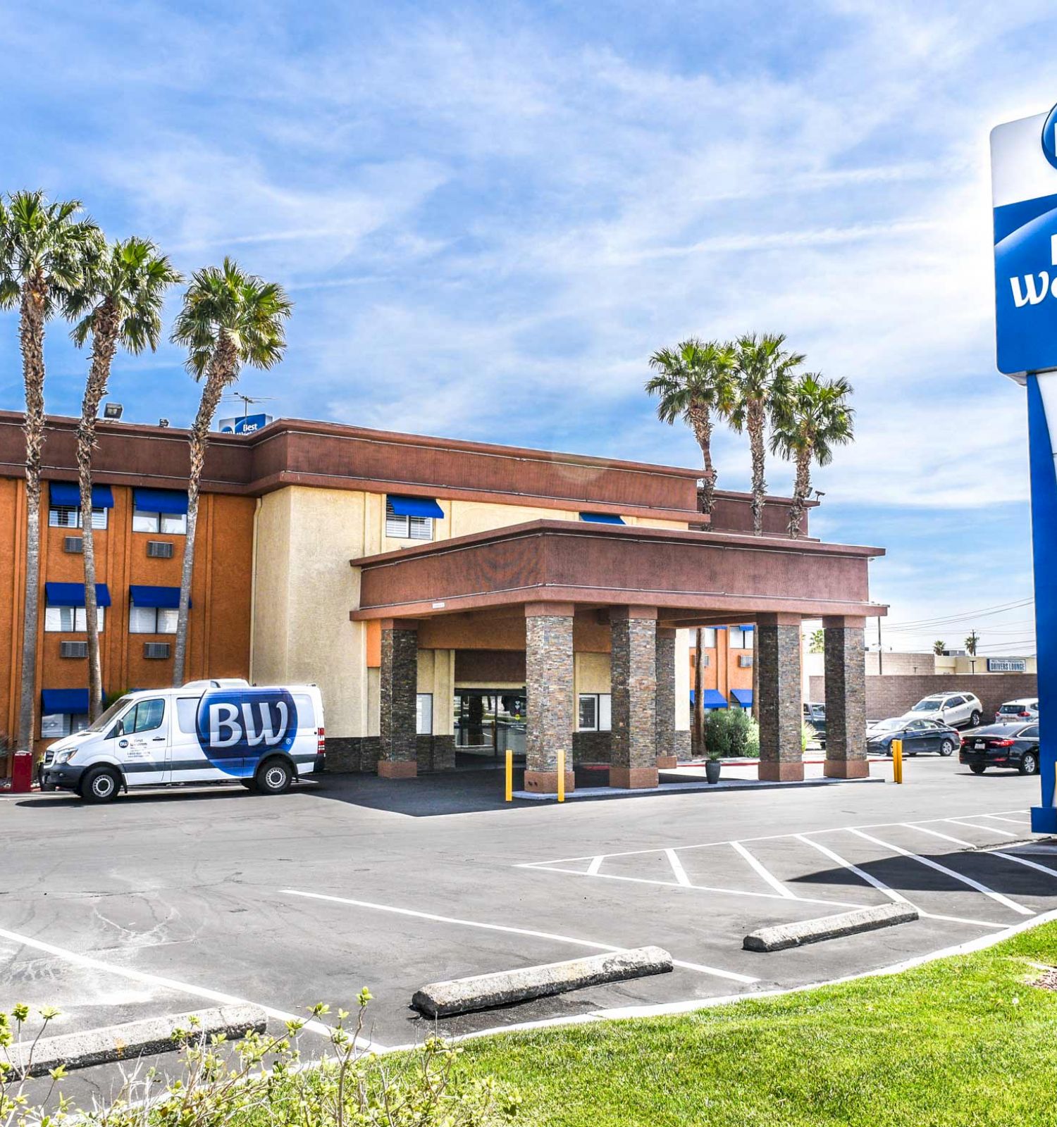 This image shows a Best Western hotel with a van parked outside. The building has palm trees around and clear skies above, ending the sentence.