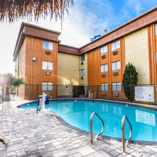 This image depicts an outdoor swimming pool area with lounge chairs, striped towels, and a shaded seating area next to a multi-story building.