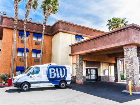 The image shows a hotel with a BW-branded delivery van parked under the entrance canopy, palm trees, and a blue sky in the background.